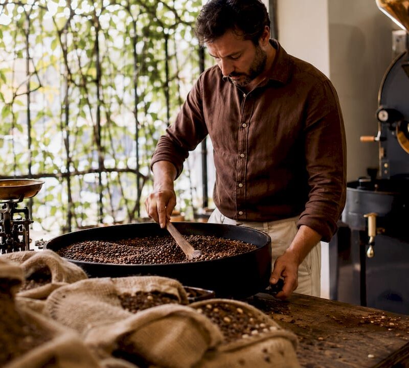 Barista stirring freshly roasted coffee beans in roasting workspace